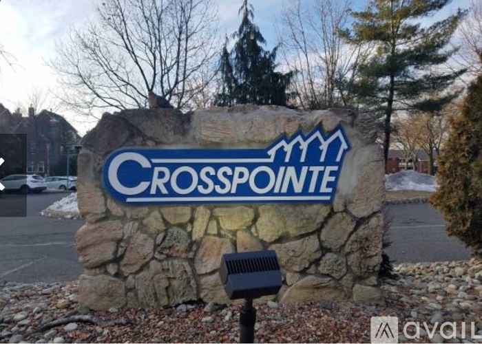 A stone wall with a sign that says "Crosspointe" in front of a parking lot.
