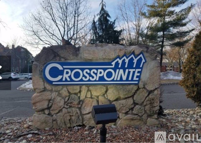 A stone wall with a sign that says "Crosspointe" in front of a parking lot.