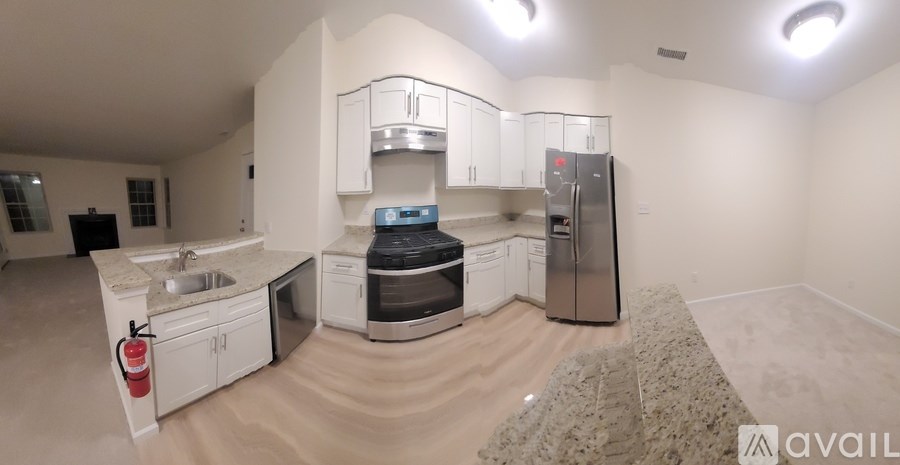 A kitchen with a sink, stove, and refrigerator in a room with beige carpeting.