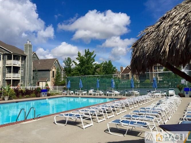 A pool with sun loungers and a thatched roof building in the background.