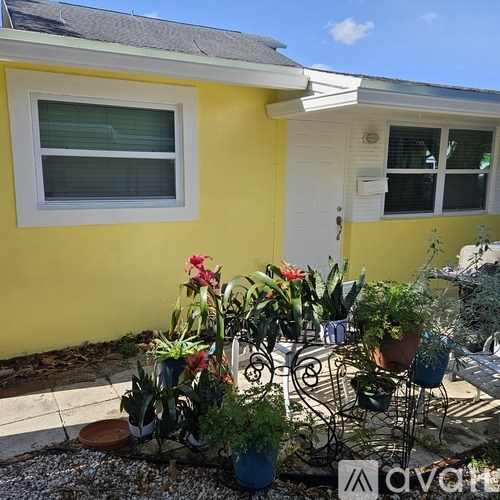 A yellow house with a white door and windows, and a garden with potted plants.