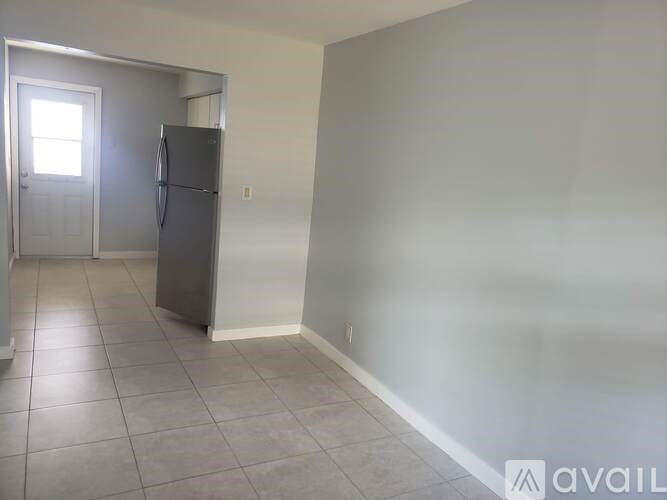 A room with a refrigerator and a door leading to another room.