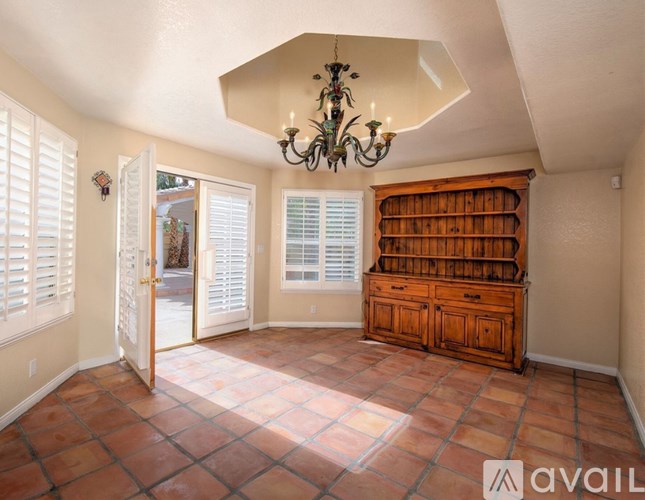 A room with a chandelier, a dresser, and a door leading outside.