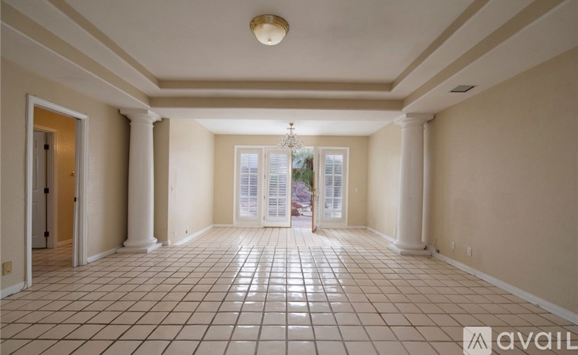 A spacious room with a chandelier, tiled floor, and a door leading to a balcony.