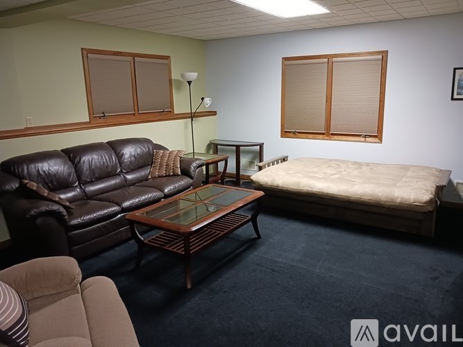 A living room with a black leather couch, a glass coffee table, and a white bed.
