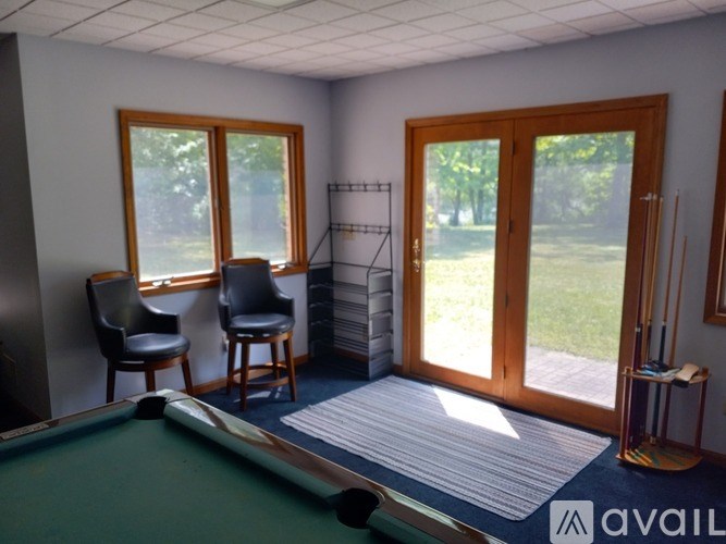 A pool table is in the middle of a room with a chair and a window.