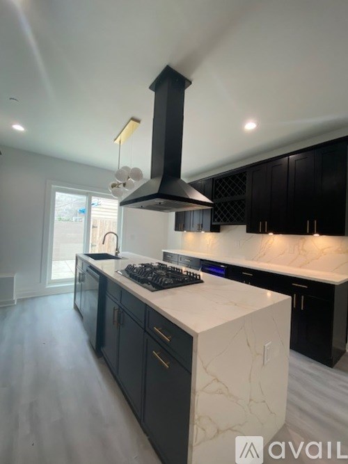 A modern kitchen with a white marble island and black cabinets.