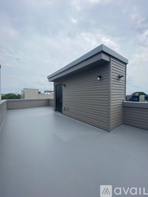 A small, grey storage shed with a closed door is situated on a white rooftop.