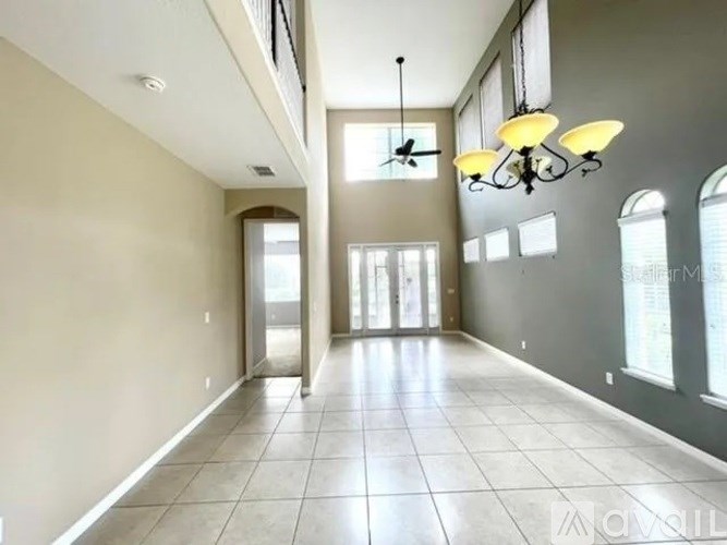 A spacious hallway with a chandelier, ceiling fan, and tiled flooring.