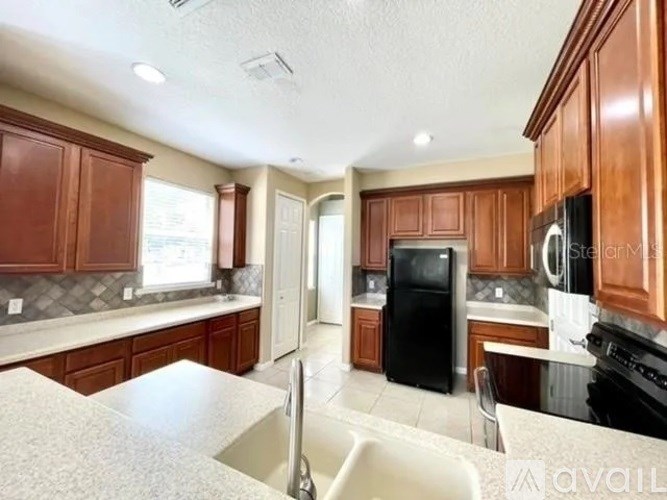 A kitchen with brown cabinets and a black refrigerator.