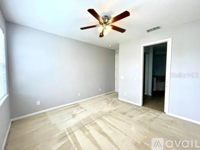 A room with a ceiling fan and light fixture, and a doorway leading to another room.