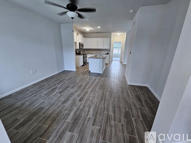 A spacious room with a kitchen in the background and a fan on the ceiling.