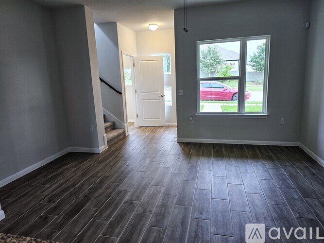 A room with a wooden floor and a window overlooking a red car.
