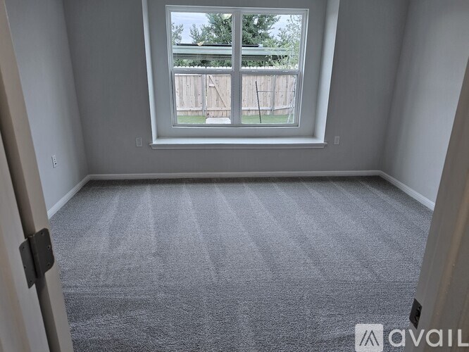 A room with a carpeted floor and a window overlooking a fence.