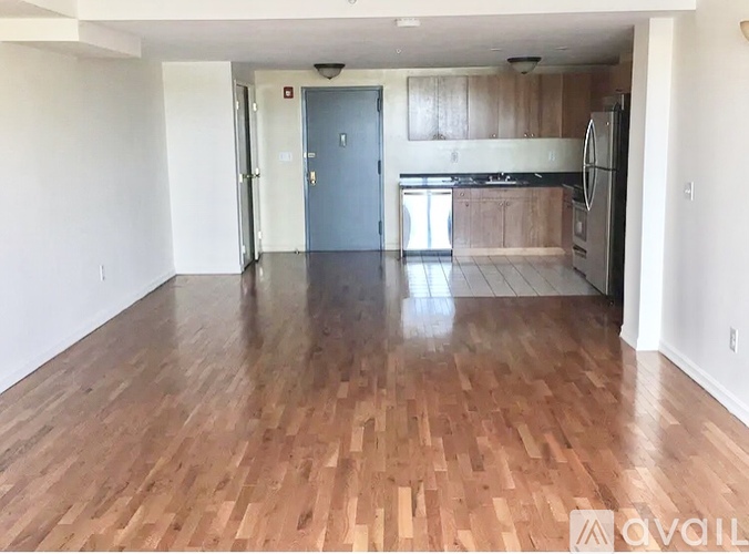 A spacious room with wooden flooring and a kitchen area in the background.