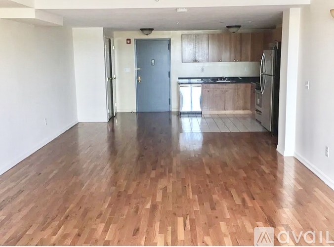 A spacious room with wooden flooring and a kitchen area in the background.