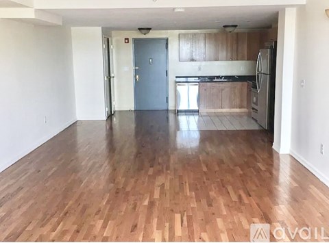 A spacious room with wooden flooring and a kitchen area in the background.