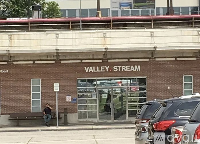 A man is sitting on a bench outside of the Valley Stream train station.