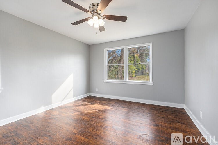 A room with a ceiling fan and a window showing trees outside.