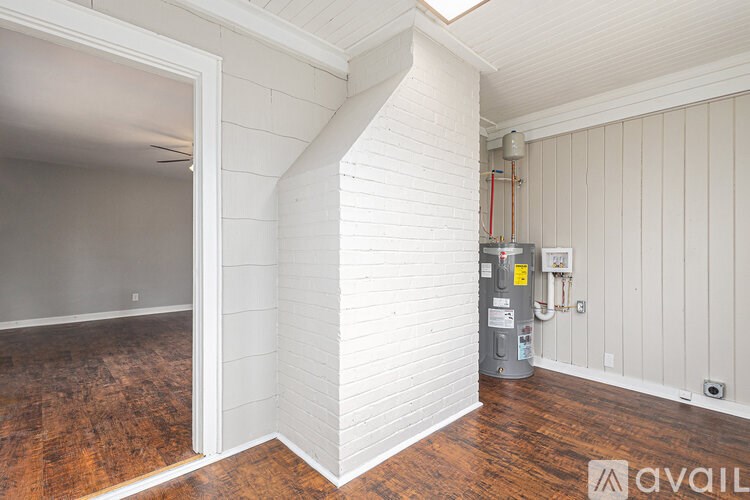 A room with a wood floor and a white wall with a doorway leading to another room.
