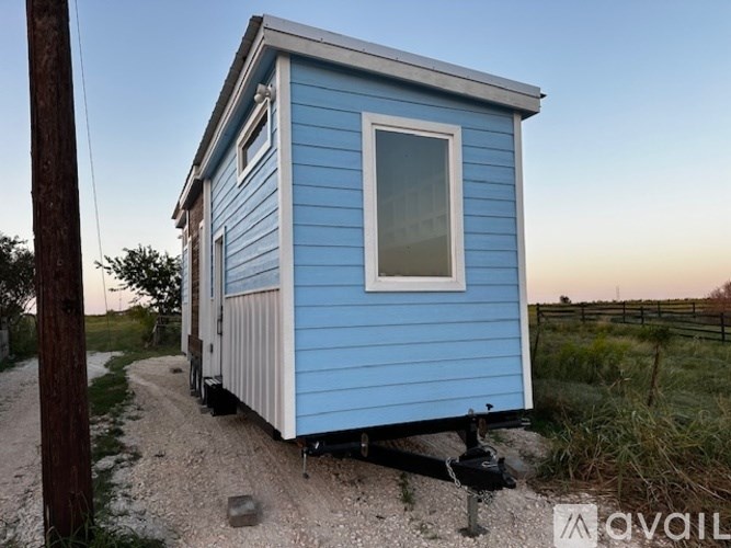 A blue house with a white window is parked on a gravel road.