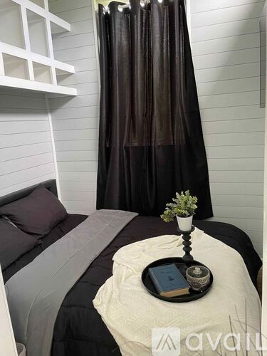 A bedroom with a bed, a nightstand with a book and a flower on it, and a window with curtains.