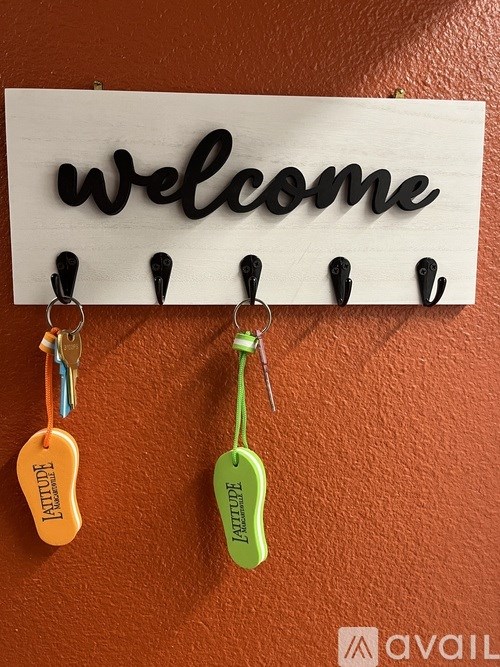 A white sign with the word "welcome" hangs on a wall with four keychains below it.