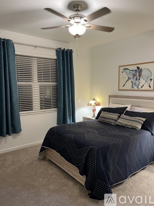 A bedroom with a bed, a ceiling fan, and a painting of a horse.