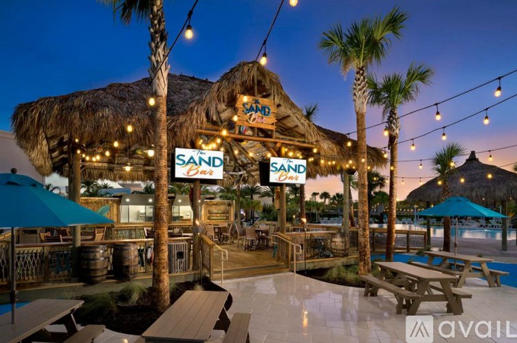 A beach bar named SAND Bar with a thatched roof and palm trees.