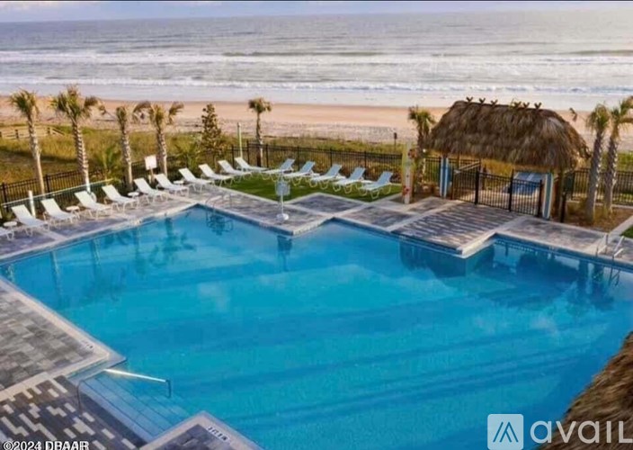 A large outdoor swimming pool with lounge chairs and a thatched roof hut overlooking the beach.