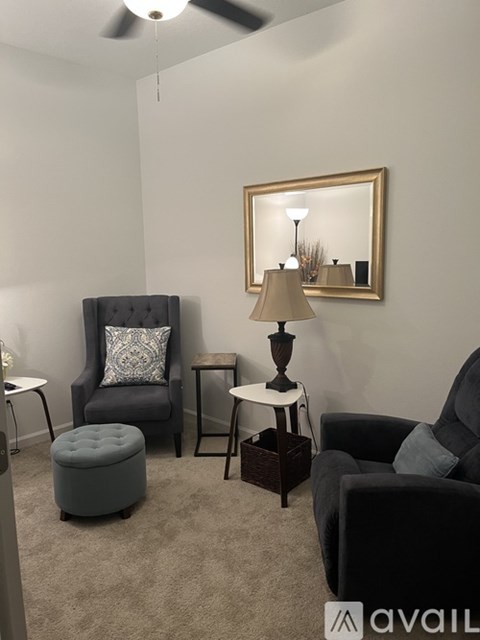 A living room with a grey armchair, a grey ottoman, a small table with a lamp and a mirror.