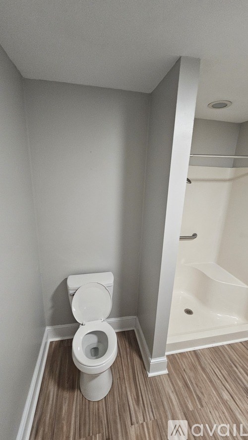 A white toilet in a small bathroom with wood flooring.