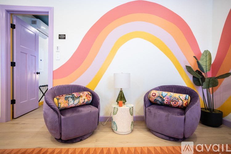 Two purple chairs with colorful cushions in front of a rainbow wall design.