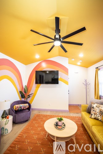 A living room with a yellow couch, a white coffee table, and a TV mounted on the wall.