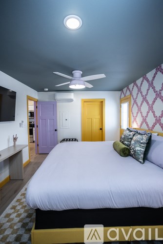 A bedroom with a bed, a ceiling fan, and a window with a purple door.