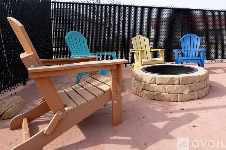 A wooden chair is in the foreground of a photo with a fire pit and other chairs in the background.