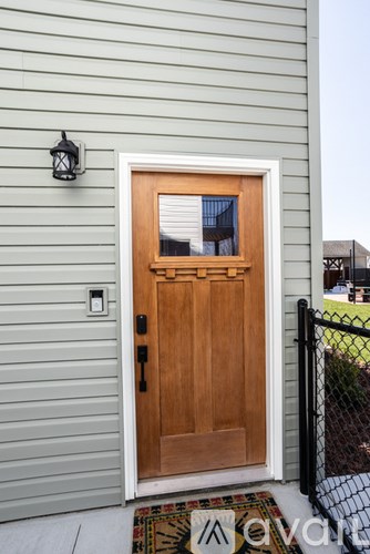 A wooden door with a glass panel is flanked by a black fence and a light grey wall.