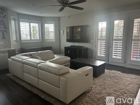 A living room with a white leather sofa and a flat screen TV mounted on the wall.