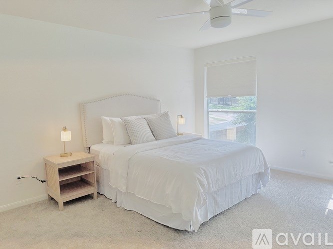 A bedroom with a large bed, a nightstand with a lamp, and a window with a view of the outside.