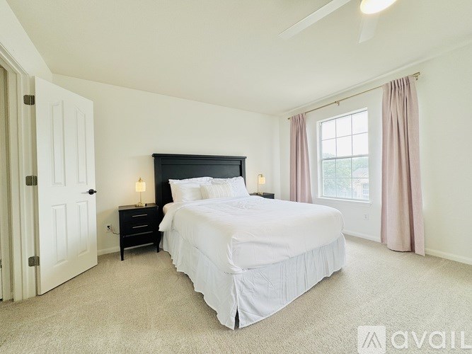 A bedroom with a large bed, a window with pink curtains, and a ceiling fan.