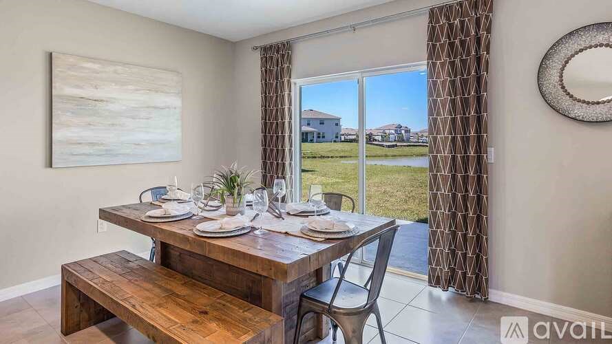 A dining area with a wooden table and chairs, a painting on the wall, and a view of the outdoors through a window.