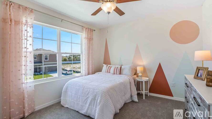 A bedroom with a large bed, a ceiling fan, and a window with a view of the outdoors.