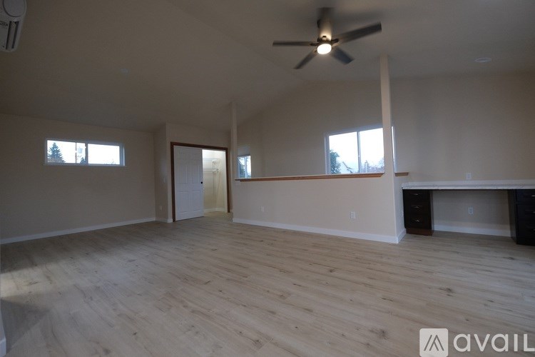 A spacious room with a ceiling fan and light, hardwood floors, and a large window.