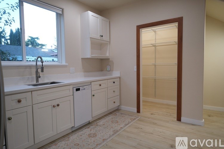A kitchen with white cabinets and a window overlooking a tree-covered hillside.