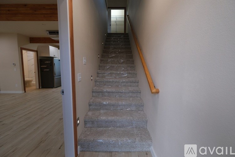 A staircase with a wooden handrail leads to a brightly lit room.