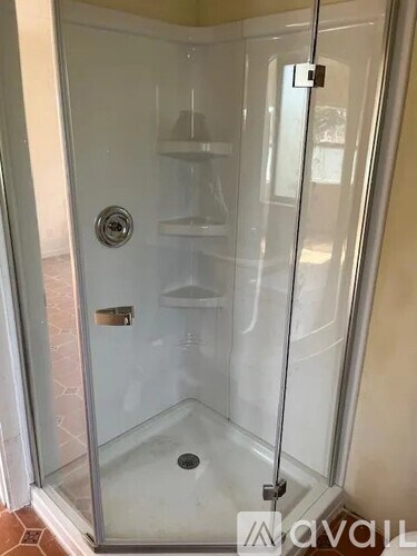 A glass shower stall with a door handle and a drain.