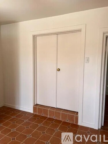 A white door with a gold handle is in a room with a tiled floor.