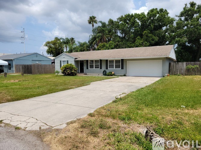 A house with a grey roof and a white garage door is surrounded by a grassy area and a driveway.