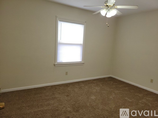 A room with a carpeted floor, a ceiling fan, and a window with blinds.