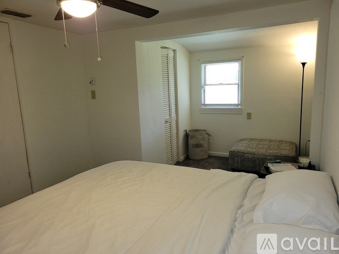 A bedroom with a bed, a window with blinds, a fan, and a lamp.